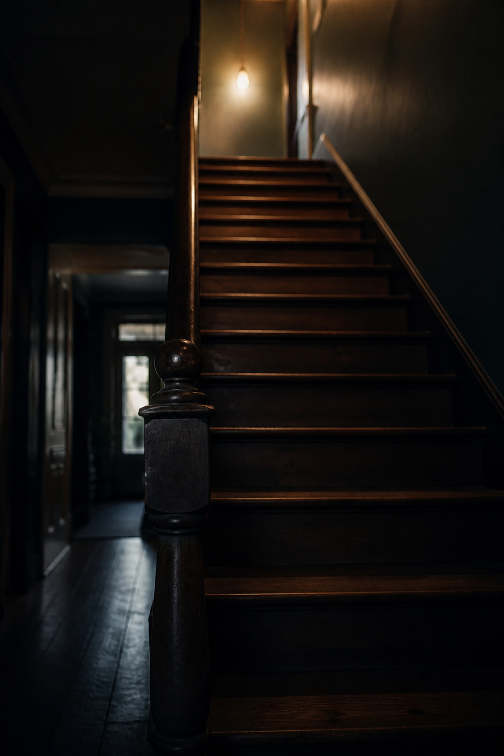 Staircase with the bottom steps in deep shadow, lit only by a single bulb at the top landing, showing an under-lit stairwell