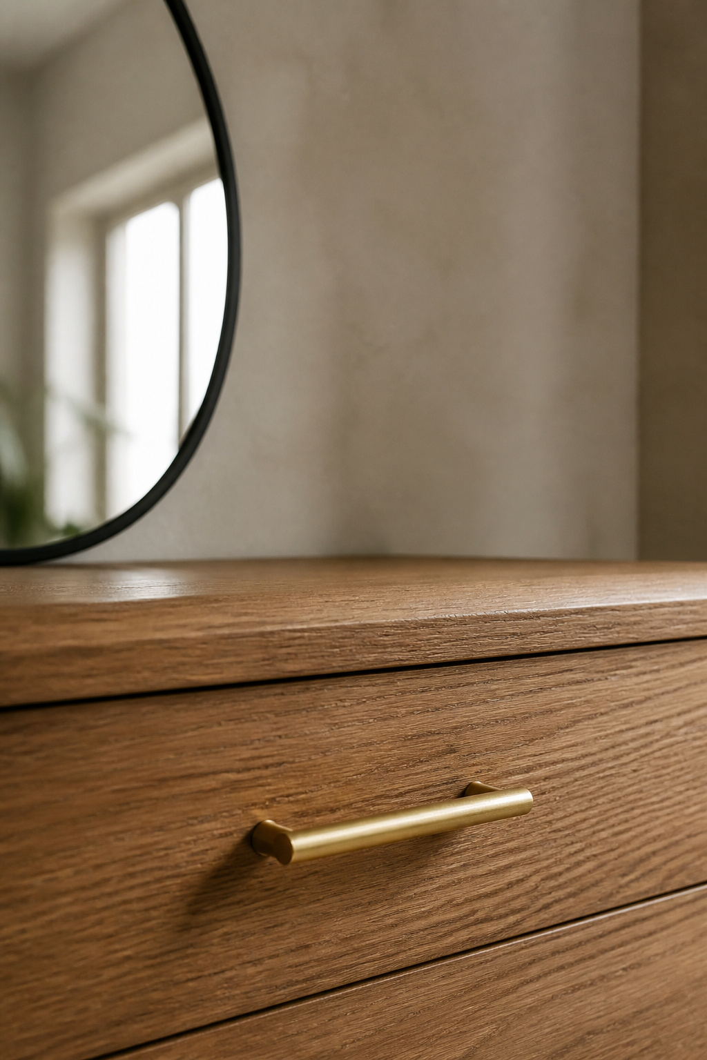 Warm oak vanity drawer front with a new brushed-brass pull beneath the edge of a matte black-framed mirror