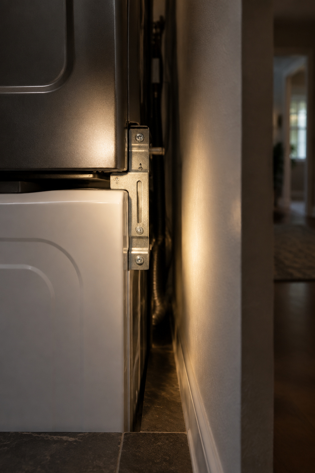 Flashlight beam illuminating the rear stacking-bracket gap between a stacked dryer and washer in a shadowed corridor