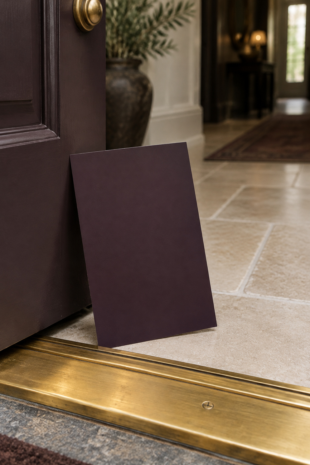 A large painted sample board of deep aubergine paint held at an open front door in daylight