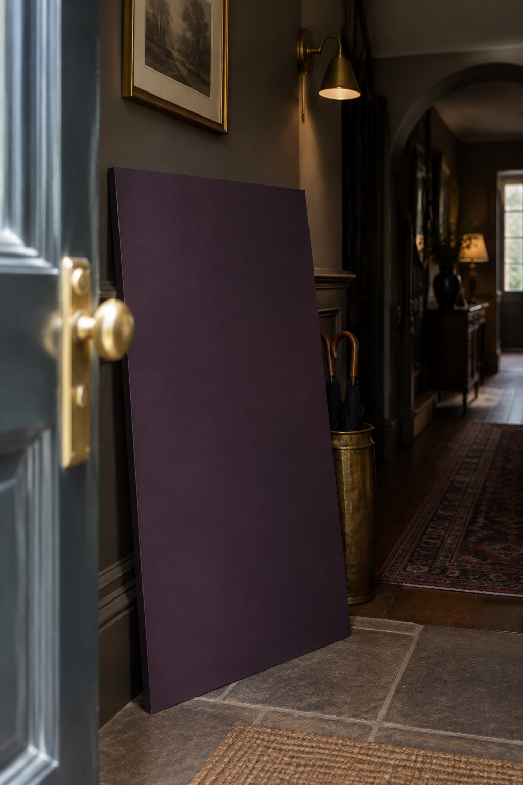 Large dark aubergine paint sample board held against an entryway wall beside an open front door in daylight