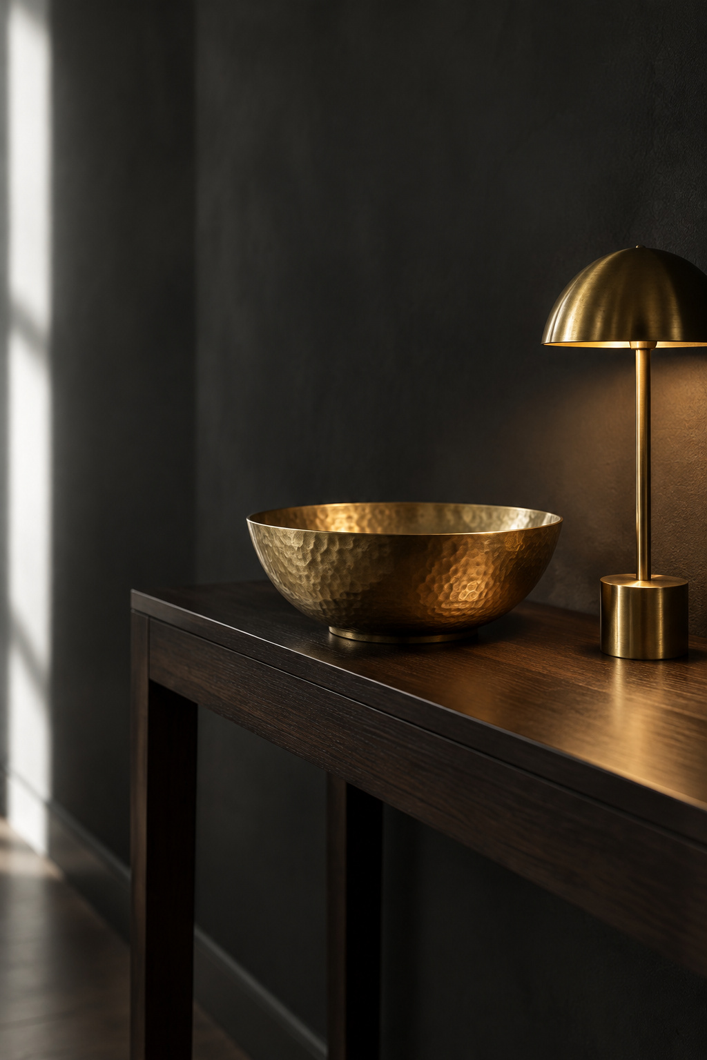 Single hammered brass bowl lit by a small accent lamp on a dark wood entryway console