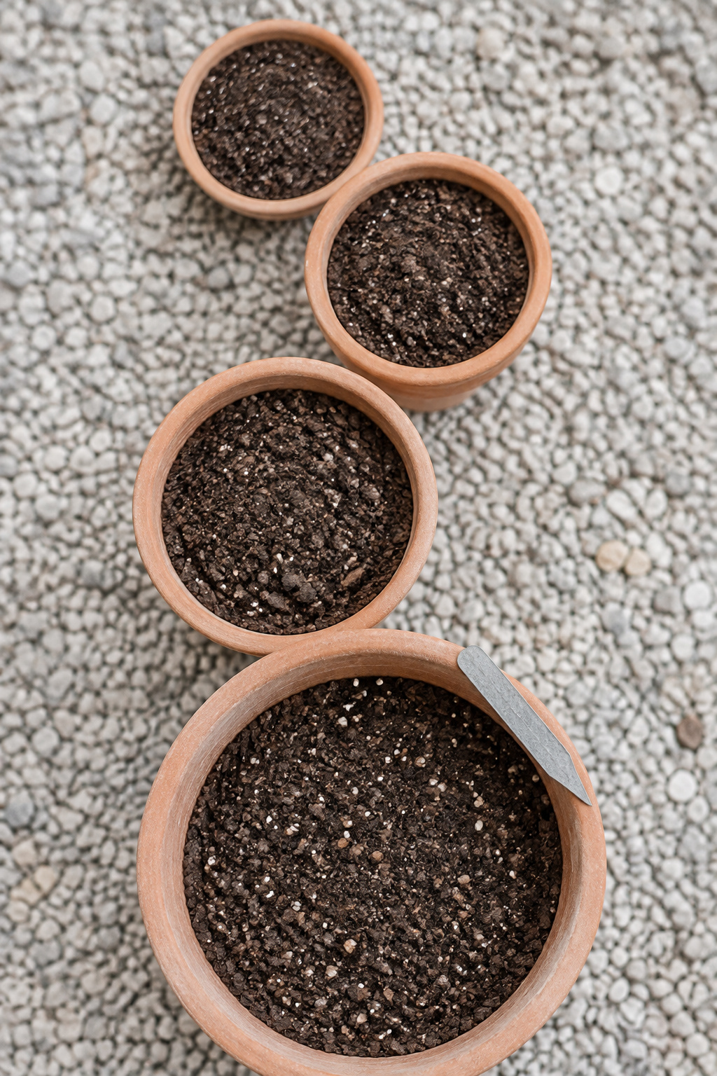Four terracotta pots of increasing size arranged top-down, from a shallow bowl planter to a deep sixteen-inch pot, each filled with soil