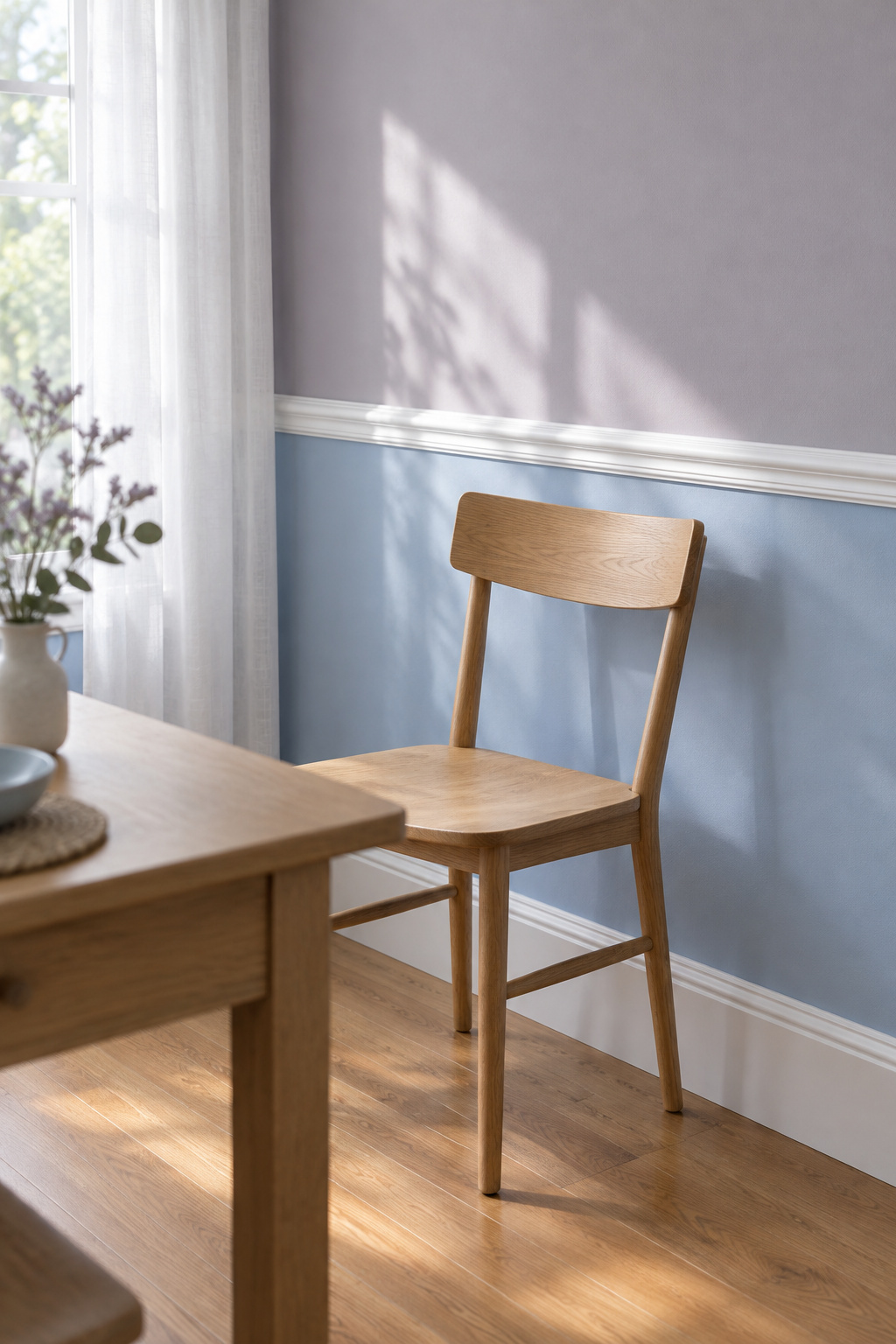 Dining room wall with a white chair rail dividing a powder-blue lower wall from a lilac-grey upper wall beside an oak chair