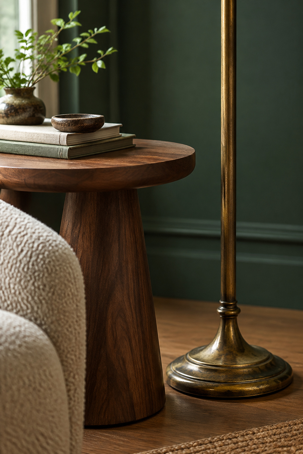Walnut side table and an unlit aged brass floor lamp base against a deep bottle-green living room wall in daylight